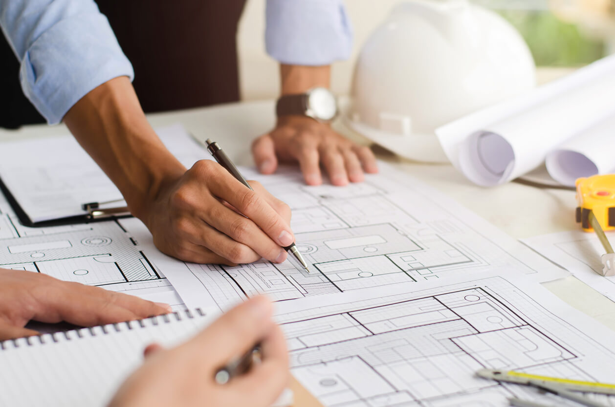 Plans d'architecte annotés sur une table, casque de chantier posé à côté