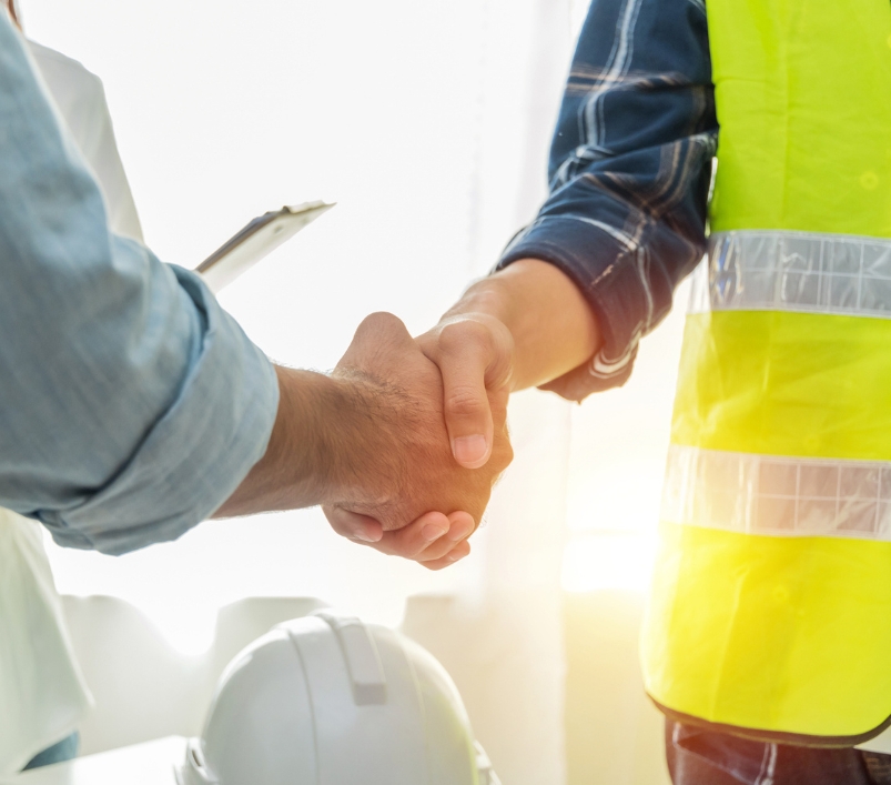 Poignée de main entre un client et un responsable de chantier, casques au premier plan